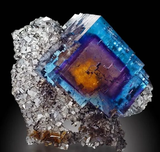Translucent fluorite cube with blue, purple, and orange color zoning on matrix.