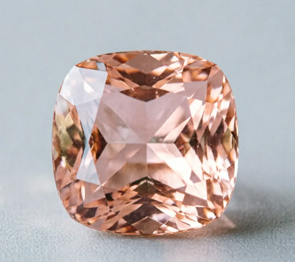 Peach-pink faceted morganite on a pale gray background.