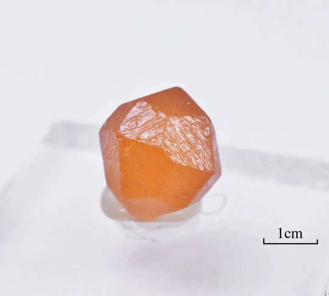 Orange rough spessartine garnet specimen with a one-centimeter scale